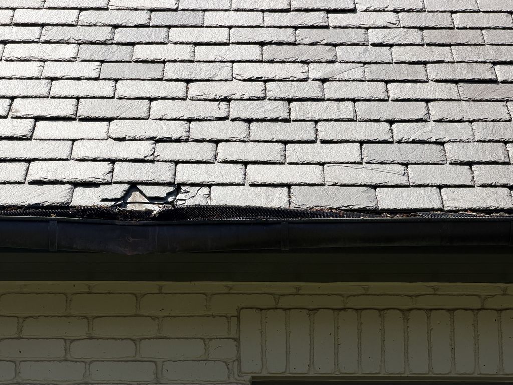 Cracked and missing synthetic slate tiles at the eave of a San Antonio roof during inspection