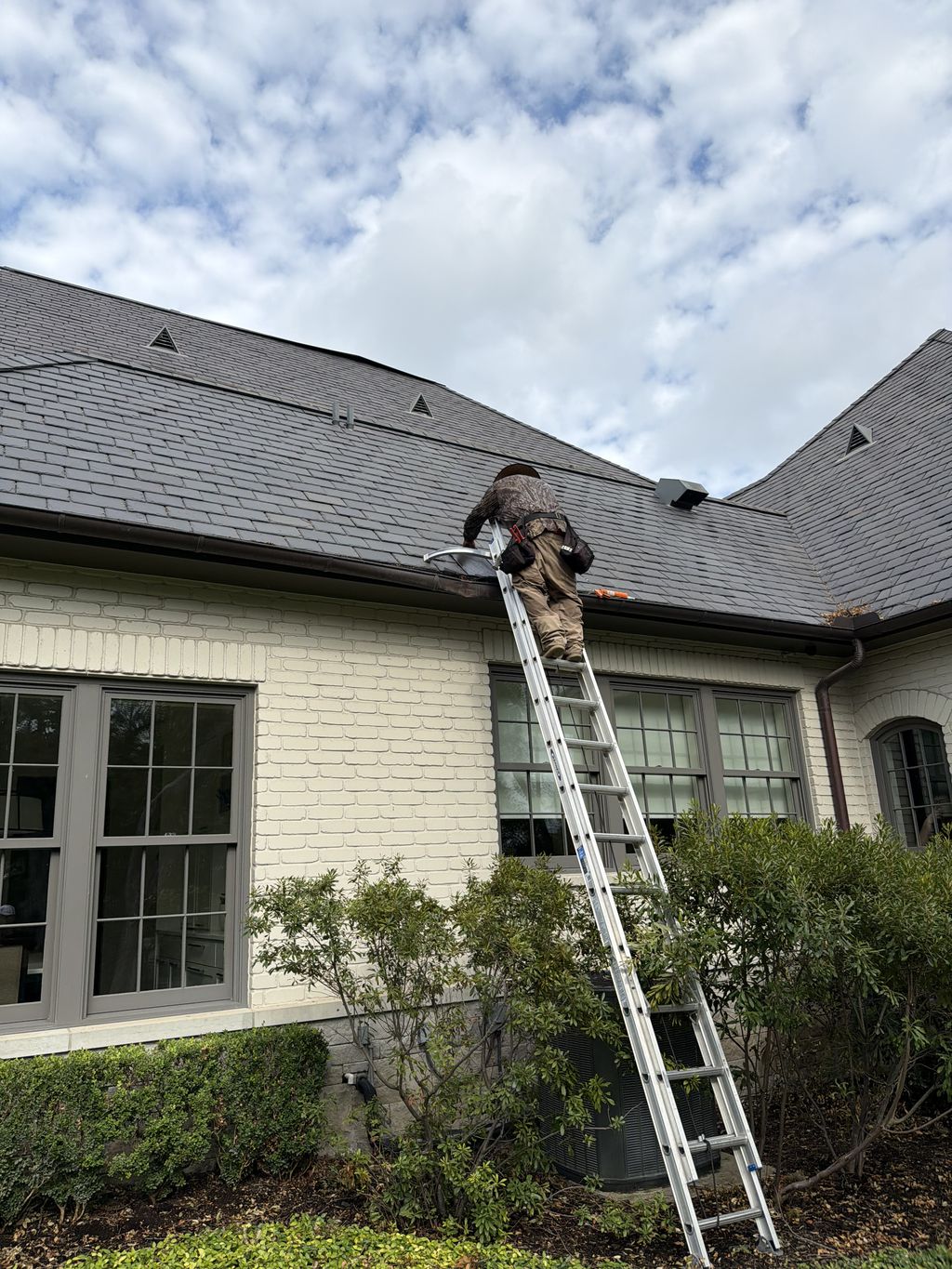 Fortem Contracting roofer on a ladder inspecting the eave and gutter line of a slate roof