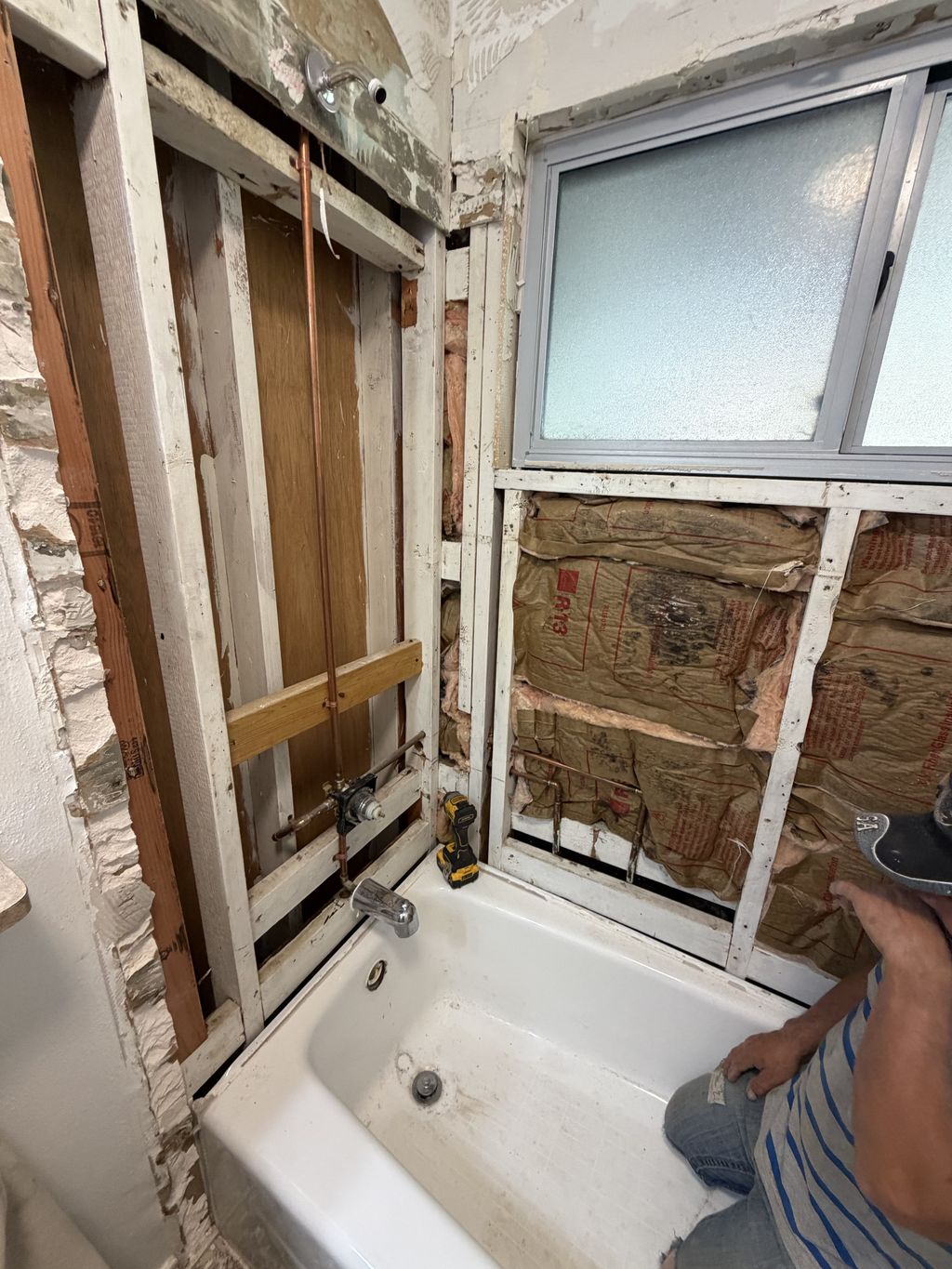 Bathroom wall opened to the studs during a tub-to-shower conversion, showing copper supply lines and old insulation